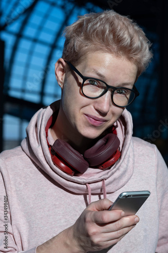 Portrait of a beautiful woman with glasses standing at the airport and writing a message with headphones