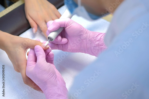 Manicurist woman removes gel shellac polish from client s nails using manicure machine  hands closeup. Manicure master is working with electric nail drill in beauty salon. Hardware manicure process.