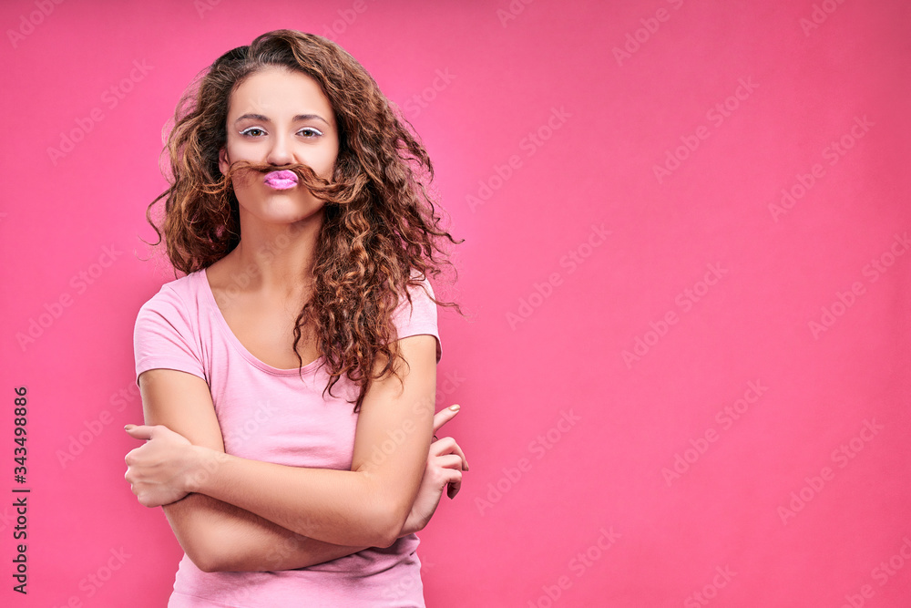 Funny young woman making mustache with hair strand isolated on pink Funny young woman making mustache with hair strand isolated on pink