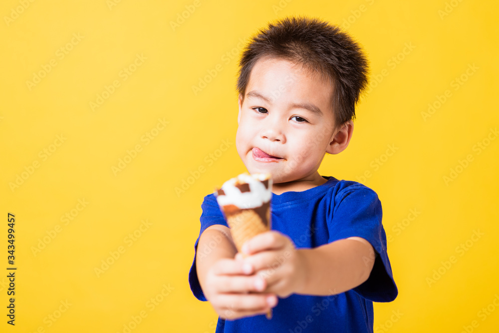 Happy portrait Asian child or kid cute little boy attractive laugh smile playing holds and eating sweet chocolate ice cream waffle cone, studio shot isolated on yellow background, summer concept Happy portrait Asian child or kid cute little boy attractive laugh smile playing holds and eating sweet chocolate ice cream waffle cone, studio shot isolated on yellow background, summer concept