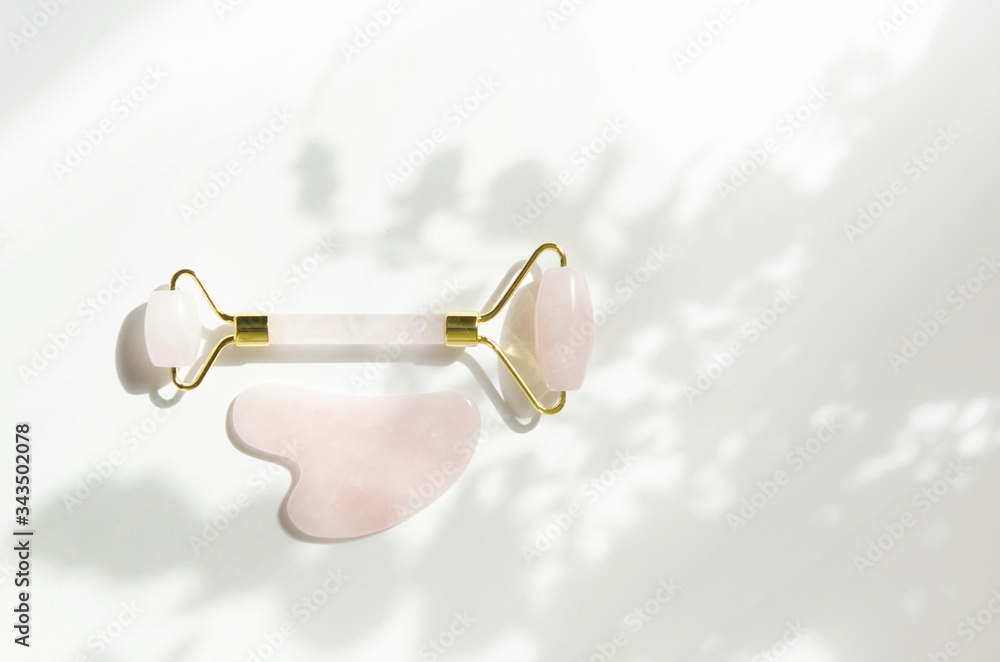 Pink Gua Sha massage tool. Rose Quartz roller. Gray shadow of the leaves on a white background. Facial skin care at home, anti-aging and lifting therapy.  - Image