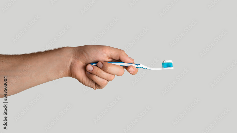 Oral hygiene. Young guy holding toothbrush with paste on light grey background, closeup. Panorama Oral hygiene. Young guy holding toothbrush with paste on light grey background, closeup. Panorama
