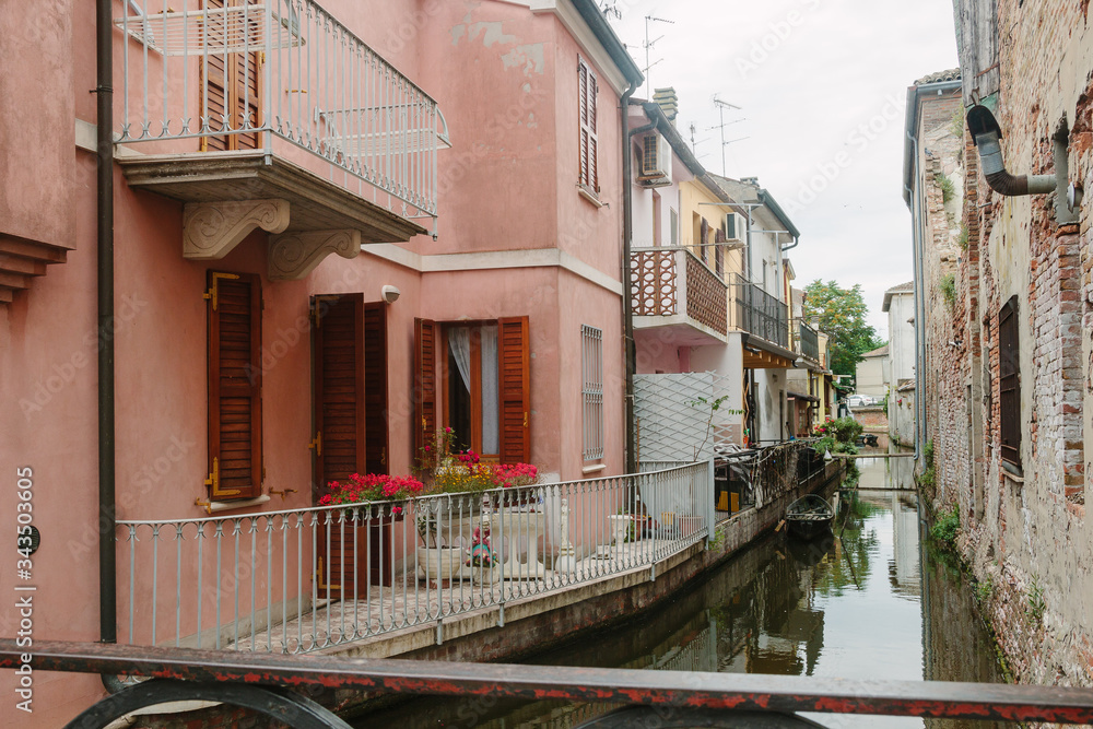 Italian street and bright pink house and water canal. Evetyday life. Inside of yard. Nobody. Middle day in Italy. Walking around in little town in Italy. Courtyard in house. Commachio.