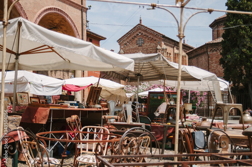 Flea market in Bologna. Old unnecessary things sell in the street. Italian flea market in sunny day. Ancient building with arch. Square with tables and chairs. Ancient furniture on the bazaar. Nobody.