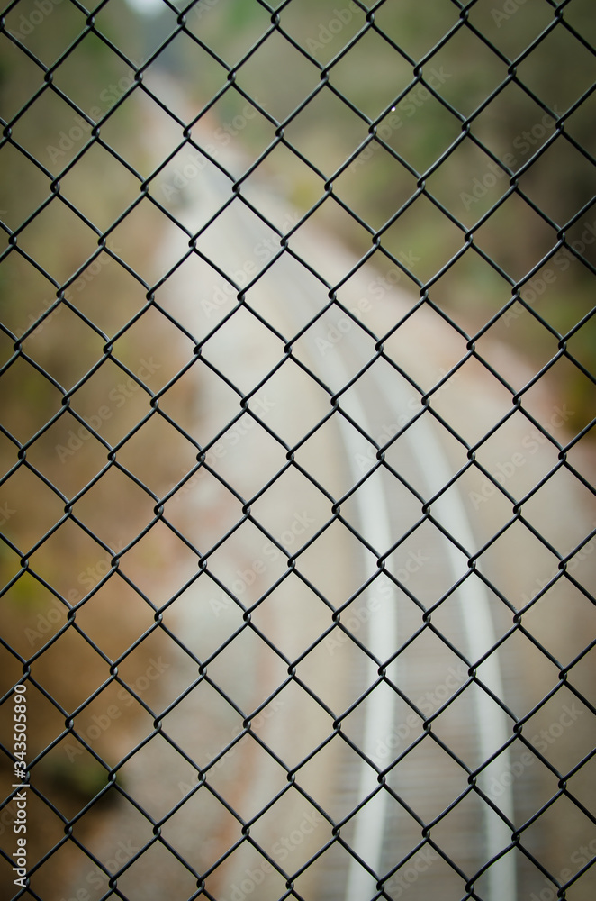 Defocused railroad tracks behind black wire fence.