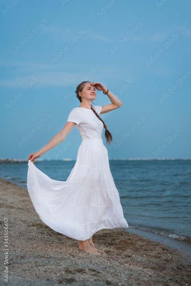 Young woman in long white dress stands on shore of sea background. Vertical frame Young woman in long white dress stands on shore of sea background. Vertical frame