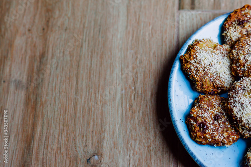 Close-up of oatmeal, banana and pure cocoa cookies with grated coconut on top on a blue plate on a wooden board