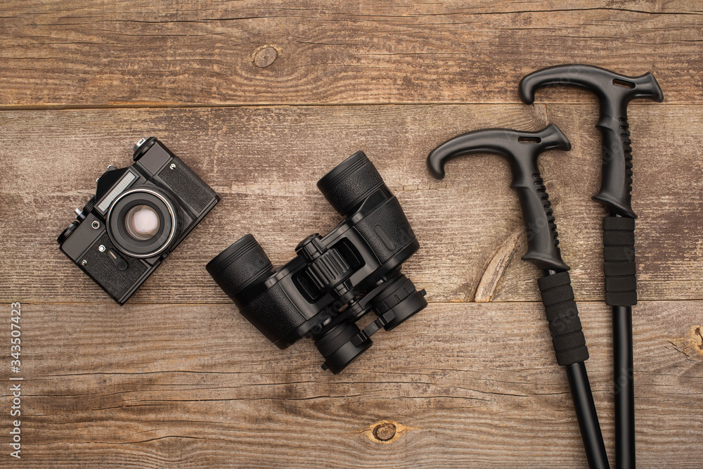 top view of photo camera, binoculars and trekking poles on wooden table top view of photo camera, binoculars and trekking poles on wooden table