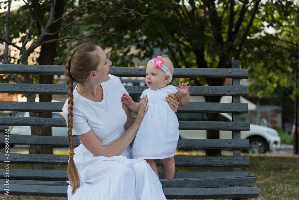 Fototapeta premium Young happy mother playing with baby girl sitting on bench in Park