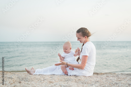 Happy young mother and small child sitting on beach. Motherhood and care