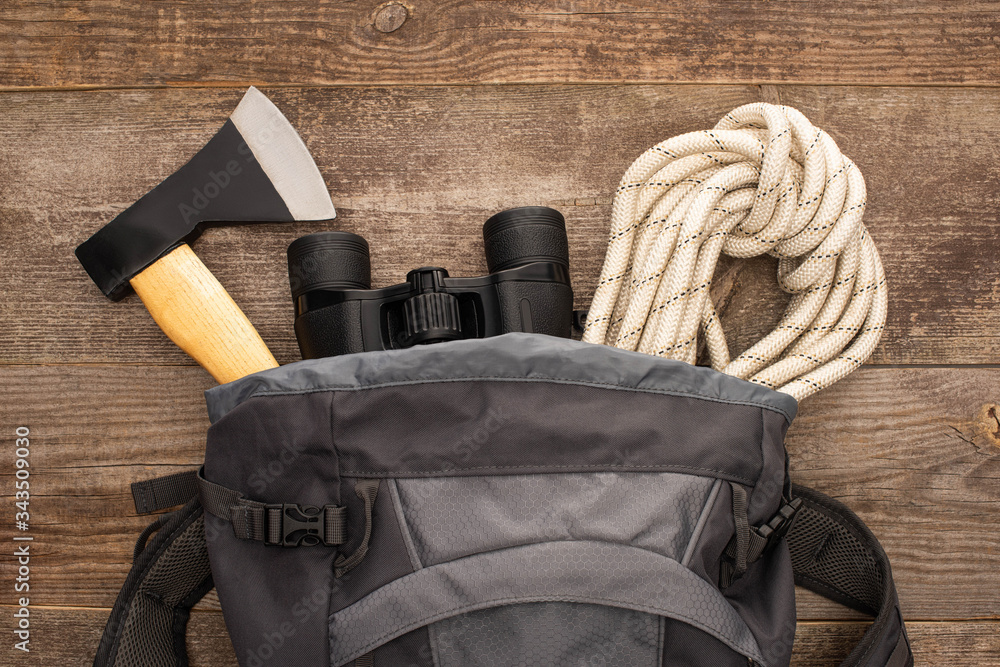 top view of backpack with axe, hiking rope and binoculars on wooden surface - obrazy, fototapety, plakaty 