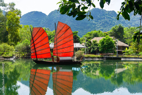 Junk. Beautiful traditional vietnamese boat with red sails on a picturesque lake in the jungle. Red sails reflected in the water.
