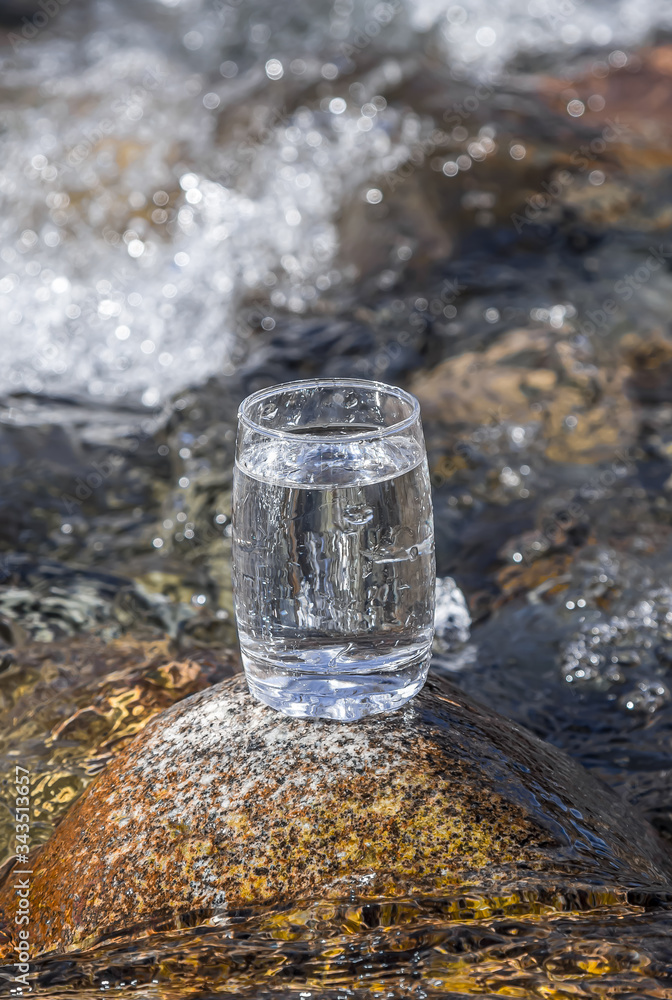 Glass cup with cold water on a background of a mountain river. Glass cup with cold water on a background of a mountain river.