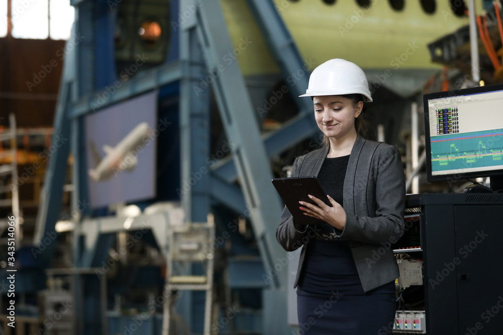 Portrait of a female factory manager in a white hard hat and business suit. Controlling the work process at the airplane manufacturer. Portrait of a female factory manager in a white hard hat and business suit. Controlling the work process at the airplane manufacturer.