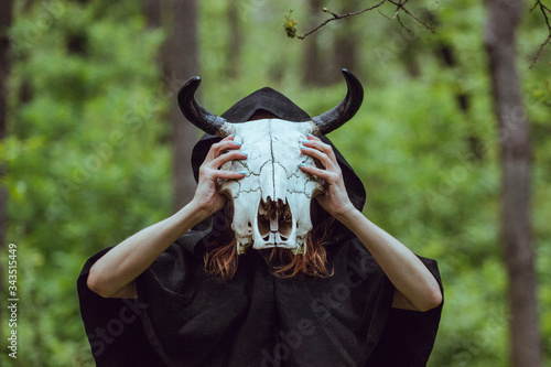 Victim with skull of the animal instead of head. Photo stylized as shooting on an old camera, with noise and imperfection of the image. Woman in forest with skull of cow occupies Occult calls to demon photo