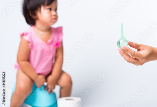 Asian little cute baby child girl training to sitting on blue chamber pot or potty her problem cannot shit and mother use Enema for help, studio shot isolated on white background, wc toilet concept photo