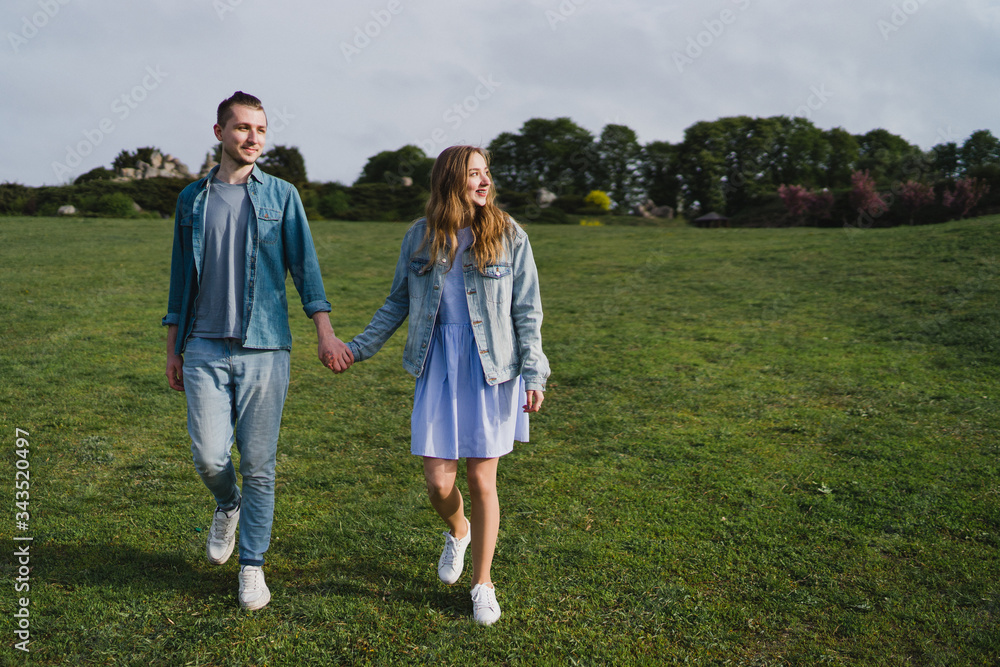 Romantic and happy caucasian couple in casual clothes hugging on the background of beautiful blooming trees. Love, relationships, romance, happiness concept. Man and woman walking outdoors together.