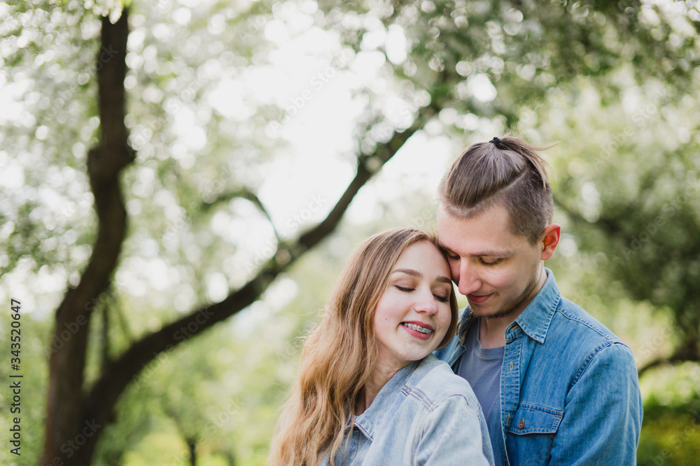 Fototapeta premium Romantic and happy caucasian couple in casual clothes hugging on the background of beautiful blooming trees. Love, relationships, romance, happiness concept. Man and woman walking outdoors together.
