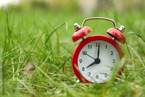 Alarm clock on green grass background. Springtime
