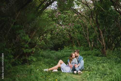 Romantic and happy caucasian couple in casual clothes hugging on the background of beautiful blooming lilac. Love, relationships, romance, happiness concept. Man and woman walking outdoors together. © anna_gorbenko