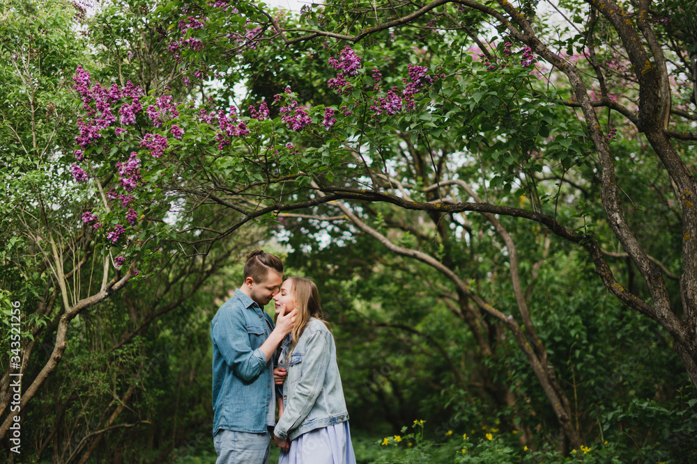 Romantic and happy caucasian couple in casual clothes hugging on the background of beautiful blooming lilac. Love, relationships, romance, happiness concept. Man and woman walking outdoors together. Romantic and happy caucasian couple in casual clothes hugging on the background of beautiful blooming lilac. Love, relationships, romance, happiness concept. Man and woman walking outdoors together.