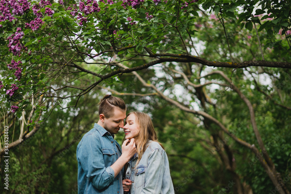 Romantic and happy caucasian couple in casual clothes hugging on the background of beautiful blooming lilac. Love, relationships, romance, happiness concept. Man and woman walking outdoors together. Romantic and happy caucasian couple in casual clothes hugging on the background of beautiful blooming lilac. Love, relationships, romance, happiness concept. Man and woman walking outdoors together.