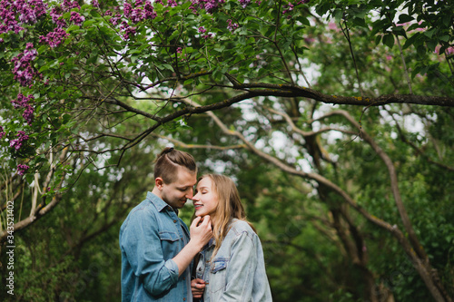 Romantic and happy caucasian couple in casual clothes hugging on the background of beautiful blooming lilac. Love, relationships, romance, happiness concept. Man and woman walking outdoors together.