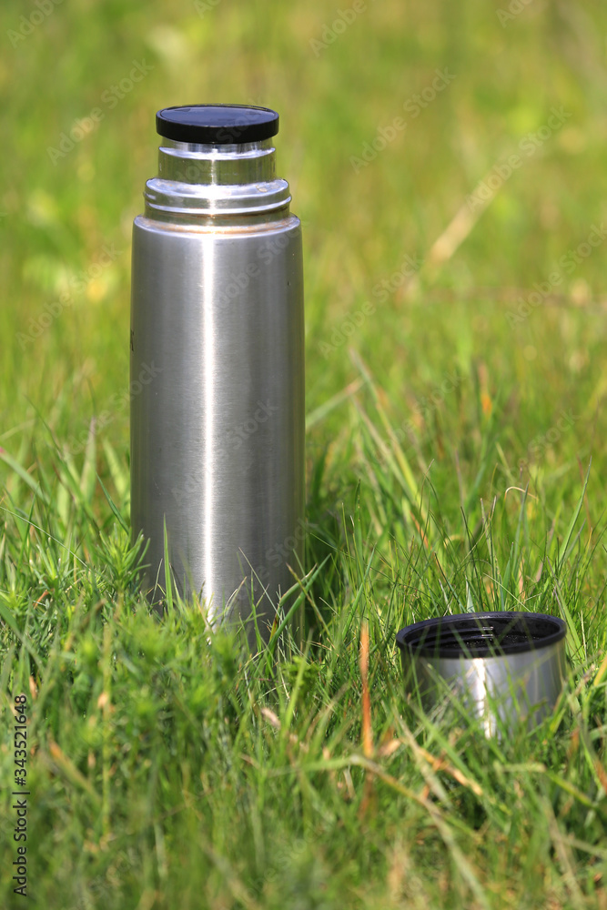 steel thermos with a cup on the grass steel thermos with a cup on the grass