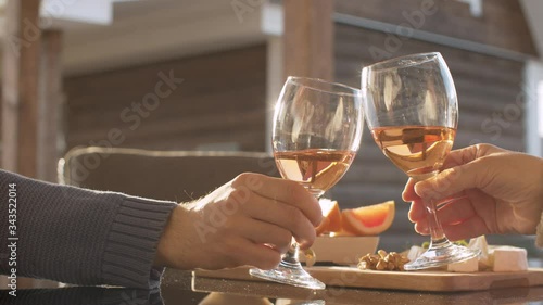 Close up hands of two people clinks wine glasses. Cheese, fruits and nuts on the table outdoors. Spring, the evening sun beautifully shining on the glass.