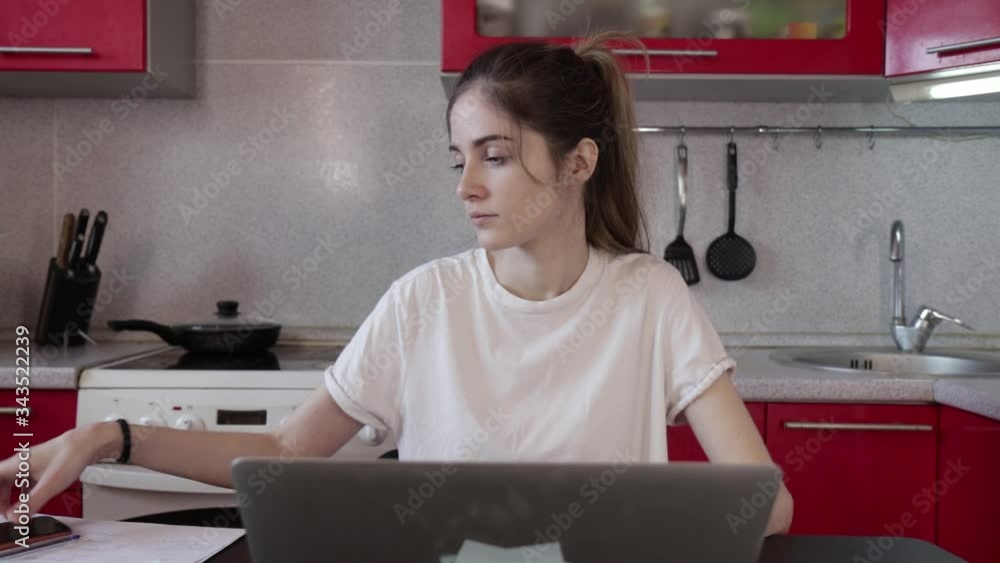 The girl works at home on a laptop, hears a phone call and answers it The girl works at home on a laptop, hears a phone call and answers it