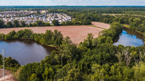 Aerial view of farmland fields and two ponds surrounded by a forest next to a residential subdivision with many houses