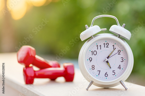 Time 5 oclock morning for exercising alarm clock and dumbbells on green natural background outside, sport and workout concept photo