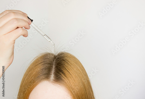 A glass pipette with a hair growth agent is applied to the parting of the hair, red hair. New hair is growing. Hair care. Light background, free space for text.