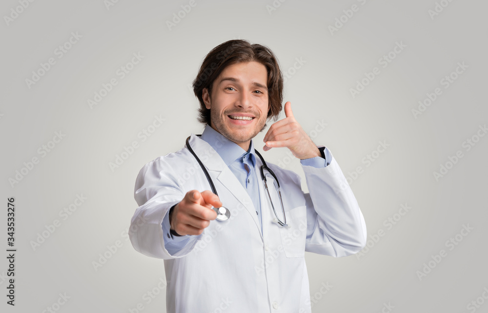 Positive medical specialist pointing at camera and showing call gesture Positive medical specialist pointing at camera and showing call gesture