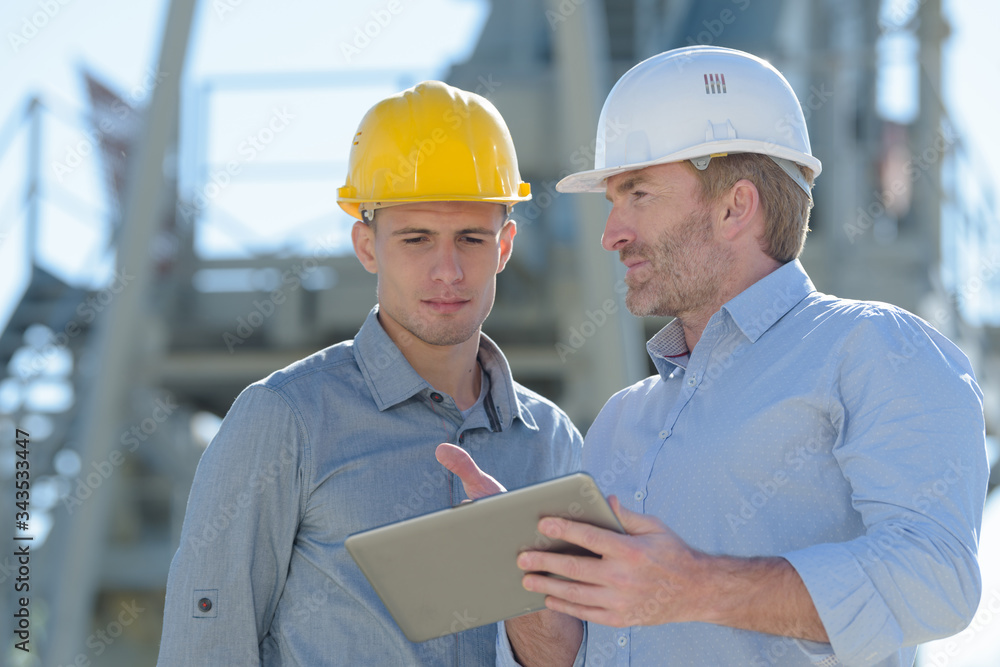 architect and apprentice with digital tablet looking away architect and apprentice with digital tablet looking away