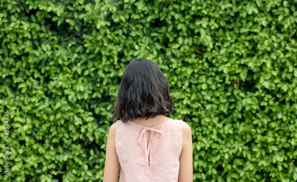 A woman with short hair and pink dressstanding on the background of the Green trees surface. a green natural background. feeling Alone and scared.vintage. Copy space.
