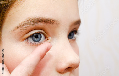 Little girl child putting contact lens into her eye closeup photo