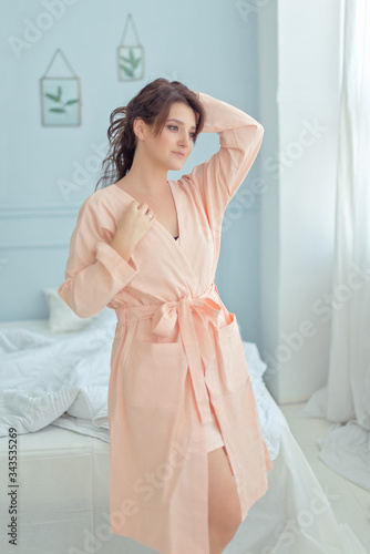 Beautifull brunette woman with long hair in a pink linen nightgown stays over her bed