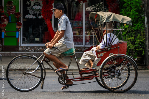 Männlicher Rikschafahrer transportiert einen Passagier auf der Straße in Bangkok Thailand photo