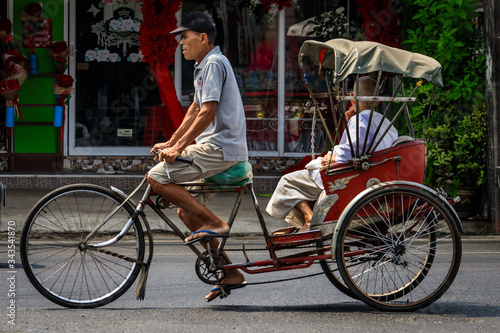 Männlicher Rikschafahrer transportiert einen Passagier auf der Straße in Bangkok Thailand
