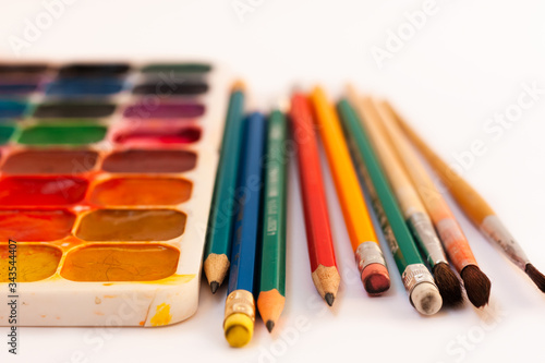 Watercolor paint, brushes, pencils well used on white background. Back to school, home schooling concept.