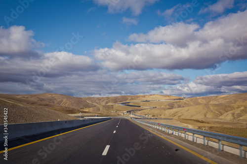 Asphalt road and bright blue sky with fluffy clouds . Empty desert asphalt road from low angle with mountains and clouds on background. road, red desert landscape . Open road with blue clouds . © Adil