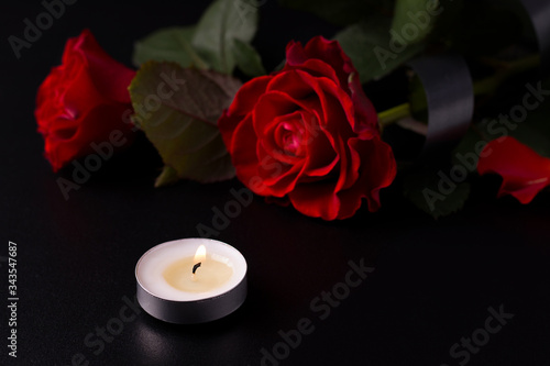 Red flowers on a black background next to candles. The concept of death and mourning. Copy space
