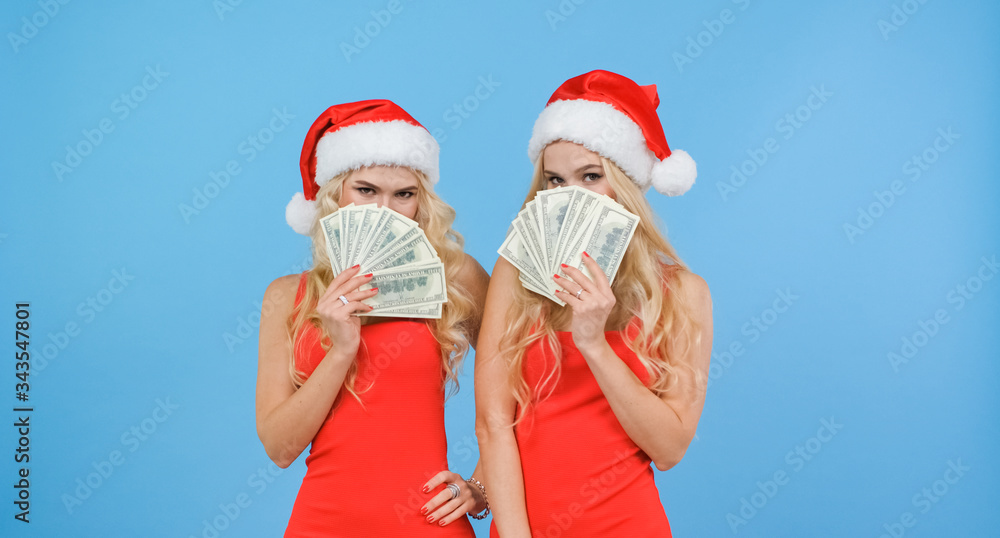 Obraz premium Twin girls in Santa hats cover their faces with a fan of dollars.