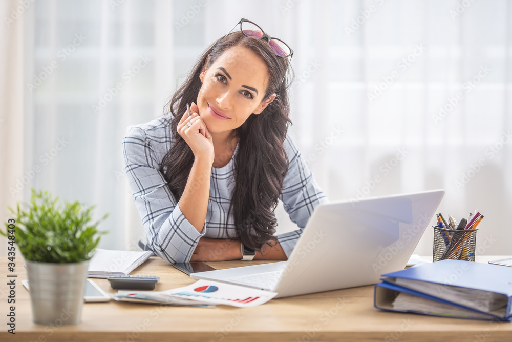 Smiling woman with titled head leaned on her hand sitting at her office desk Smiling woman with titled head leaned on her hand sitting at her office desk