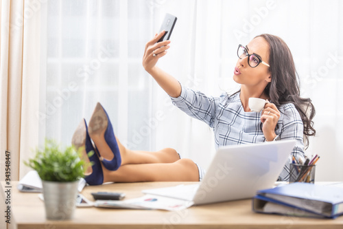 Lazy secretary with her feet up taking a selfie with a coffee in her hand