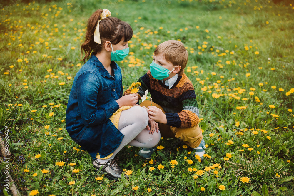 Fototapeta premium Children in medical masks cut dandelions in the garden. The concept of protection against coronovirus and social distance