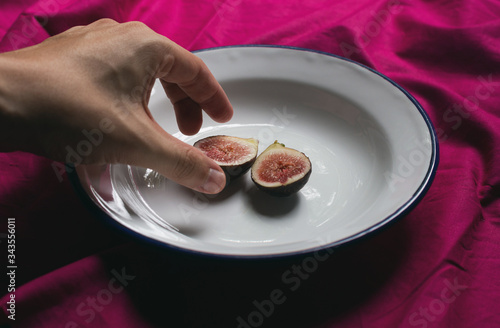 hand holding a portion of fig on an antique plate, still life style with a purple background