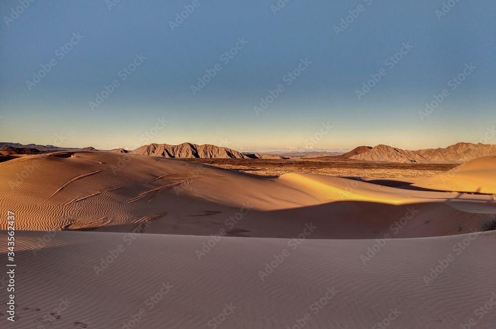 Sand dunes in desert landscape at sunset with mountains