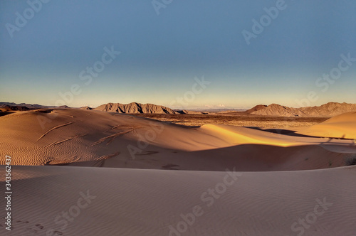 Sand dunes in desert landscape at sunset with mountains